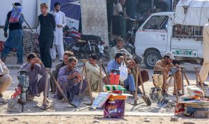 A group of labourers with their tools sitting along the roadside waiting to be hired for daily wage work.