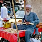 An aged man cutting sugarcane into pieces at his roadside setup for sell