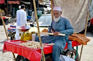 An aged man cutting sugarcane into pieces at his roadside setup for sell