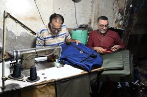 A tailor stitching school and luggage bags at his workplace.