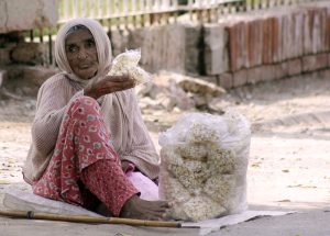 A nomadic woman cooks over an open flame as families rest on cots in a makeshift shelter, demonstrating the resilience of displaced people in difficult circumstances
