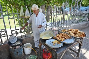 An old vendor is preparing traditional food item for customers at his roadside setup in front of Zulfiqar Bagh