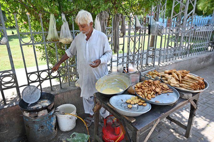 An old vendor is preparing traditional food item for customers at his roadside setup in front of Zulfiqar Bagh
