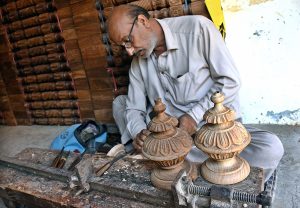 An elderly man sitting in his shop while crafting intricate designs on wood.