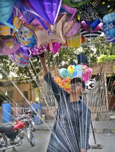 A street hawker wandering along the roadside to sell colourful balloons to earn for livelihood at satellite market