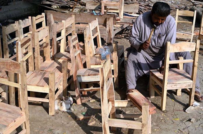 A carpenter is busy making small wooden chairs for children at his workplace near Miro Khan Road