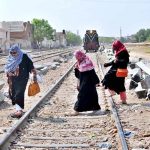 Women cross railway tracks as a train approaches in the background, highlighting unsafe pedestrian practices near railways in urban areas