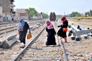 Women cross railway tracks as a train approaches in the background, highlighting unsafe pedestrian practices near railways in urban areas