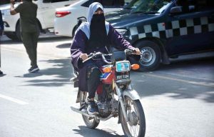 A veiled woman rides a motorcycle without a helmet on a busy road in the city.