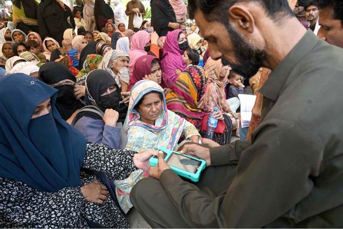 A retailer is scanning women's thumb by a machine at the Company Bagh Center to distribute money under the Benazir Income Support Program