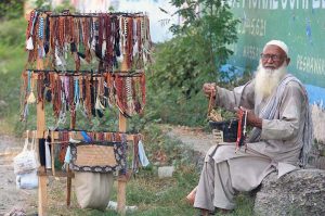 An elderly person displaying prayer beads (tabeeh) to attract the customers at Warsak Road.