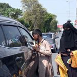A beggar boy seeks alms from a car driver while a woman selling vehicle cleaning cloths at Club Chowk junction.