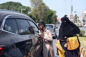 A beggar boy seeks alms from a car driver while a woman selling vehicle cleaning cloths at Club Chowk junction.