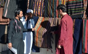 A roadside vendor displays handcrafted shawls and chadars in rich traditional hues, inviting passersby to experience the warmth and cultural heritage of Balochistan.