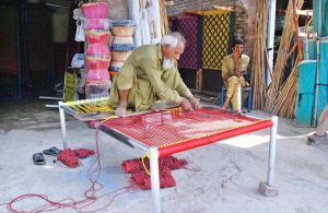 An elderly person busy knitting traditional bed (charpai) at his setup.