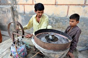 A vendor preparing a traditional sweet treat for children at a street in the city.