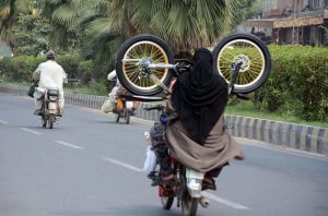 A family carries a bicycle while riding a motorcycle, maintaining balance on the city streets.