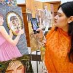 A visitor taking picture of display painting with her cell phone during celebration of International Day of Artists organized by Department of Social Welfare, Merged Districts in collaboration with Department of Art & Design UOP with the support of UNICEF at Puta Hall