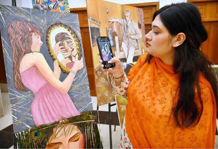 A visitor taking picture of display painting with her cell phone during celebration of International Day of Artists organized by Department of Social Welfare, Merged Districts in collaboration with Department of Art & Design UOP with the support of UNICEF at Puta Hall