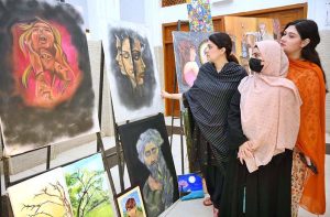 A visitor taking picture of display painting with her cell phone during celebration of International Day of Artists organized by Department of Social Welfare, Merged Districts in collaboration with Department of Art & Design UOP with the support of UNICEF at Puta Hall