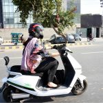 A girl rides her scooty along the road, heading towards her destination