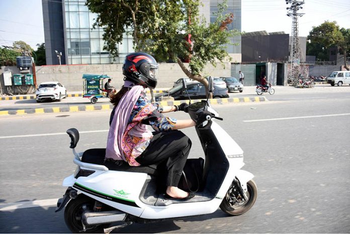 A girl rides her scooty along the road, heading towards her destination