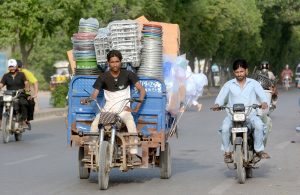 A three-wheeler driver dangerously overloads his vehicle with goods while driving on a city road.