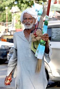 An elderly daily wage worker walks along the roadside selling brooms to earn his livelihood in the city.