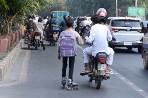 A boy skating on the road while holding onto a moving motorcycle for support, posing a serious risk of accident.