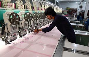 A worker adjusts an embroidery machine while designing fabric at a factory near Tarlai area in the Federal Capital.