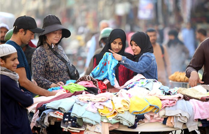 People selecting and purchasing used clothes along the roadside at Bagh Sardaran area in the city