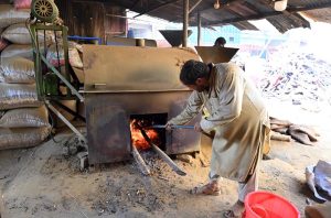 A worker feeding wood into a roasting machine to prepare peanuts at a local workplace on Lehtrar Road in the Federal Capital.