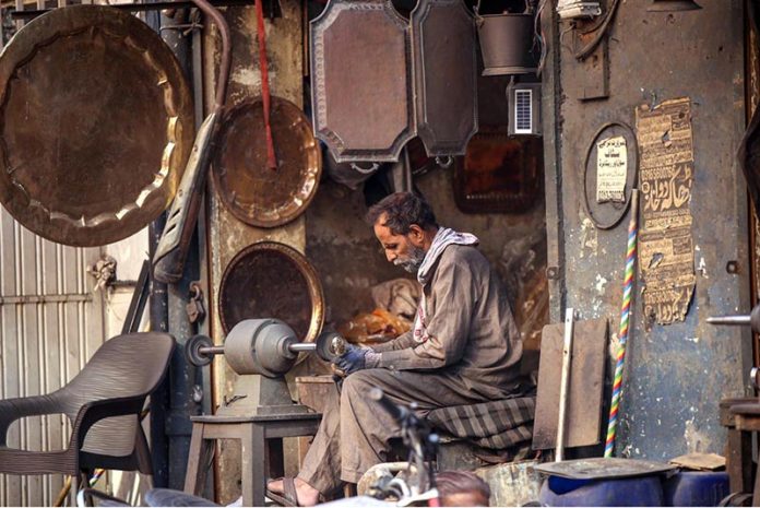 A worker busy polishing brass items at his workplace to attract customers at Bhabra Bazaar area in the city
