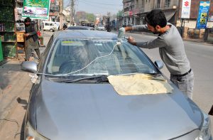 A worker uses a polishing machine to clean the windshield of a car at a roadside service point.