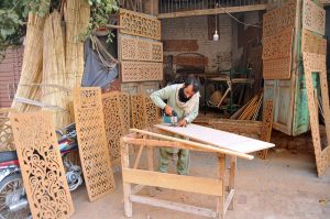 A worker skillfully carving decorative designs on a wooden sheet at his workplace.