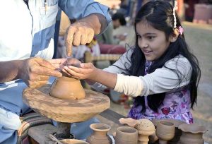 A young artisan shapes clay into small pots on a pottery wheel with the guidance of a potter during the Ten-Day annual folk festival “Lok Mela 2025” at Lok Virsa.