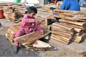 A young woodworker is busy crafting artistic designs on a wooden sheet at his workplace.