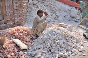 A worker is busy crushing salt for packaging at his workplace.