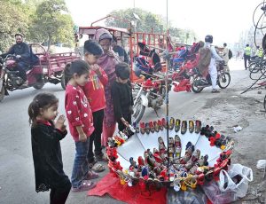 A woman along with children keenly watching children shoes beautifully decorated in umbrella at a roadside stall in the Provincial Capital.
