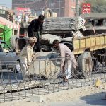 Labourers busy unloading construction material and fixing iron grills for ongoing road development work along a busy thoroughfare in the city