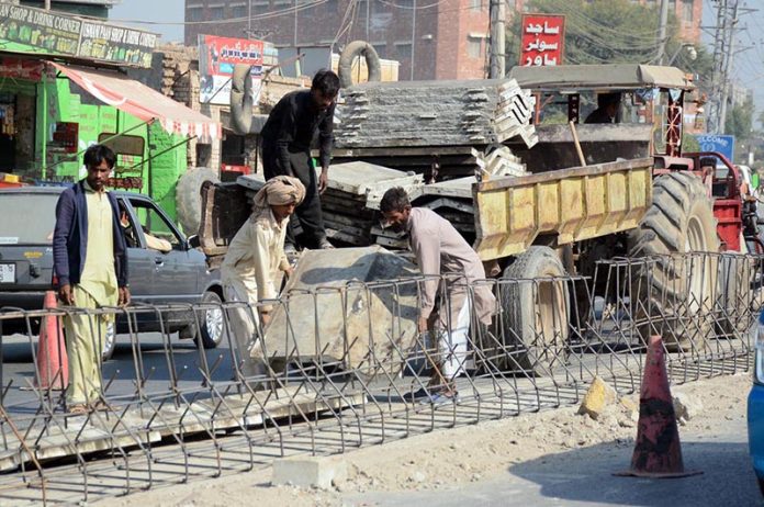 Labourers busy unloading construction material and fixing iron grills for ongoing road development work along a busy thoroughfare in the city