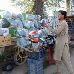 A vendor arranges and displays helmet and sunglasses at his roadside stall to attract customers and earn a livelihood for his family