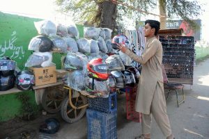 A vendor arranges and displays helmet and sunglasses at his roadside stall to attract customers and earn a livelihood for his family