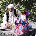 An elderly vendor sits roadside displaying colorful pinwheels and snacks for sale in the Federal Capital