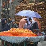 A fruit vendor waits for customers under an umbrella during the season’s first rainfall in the federal capital, as temperatures drop and a cool breeze marks the arrival of winter