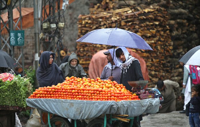 A fruit vendor waits for customers under an umbrella during the season’s first rainfall in the federal capital, as temperatures drop and a cool breeze marks the arrival of winter