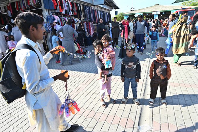 A vendor make water bubbles with a toy gun to attract children at H-9 weekly bazaar in Federal Capital