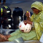 A female street vendor adjusts a helmet while waiting for customers along a roadside in the city.