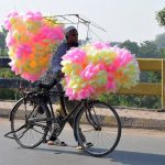 A street vendor moves along the roadside while displaying colourful cotton candy to attract customers.