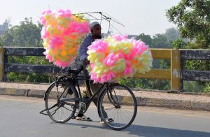 A street vendor moves along the roadside while displaying colourful cotton candy to attract customers.